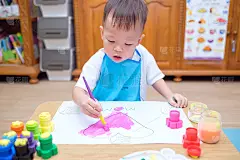 可爱的小亚洲2岁蹒跚学步的婴儿男孩用画笔和水彩画，孩子画粉红色的心，制作母亲节贺卡