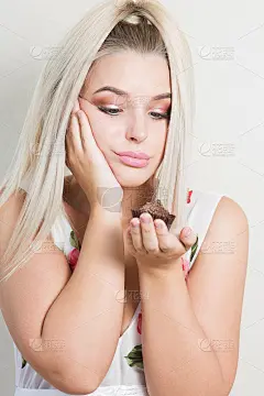 沮丧的节食年轻女人拿着美味的巧克力纸杯蛋糕