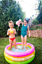 儿童夏季游戏与水池。白种人的弟弟妹妹玩的塑料玩具洒水罐泼水，充气绕儿童浴室。夏天炎热的假期穿着泳衣