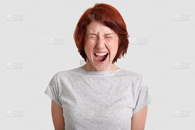 人类消极情绪、情绪和面部表情的概念。愤怒的红发女人张大嘴愤怒尖叫，穿着灰色t恤，室内模特，感觉侵略