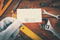 房屋建筑和维修服务。工人在木制背景上的工作工具上持有空白名片