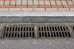 集水池格栅的格状排水系统，用于排水雨水，从路面与柏油路面，在路边与石砖瓦人行道的特写，无人。