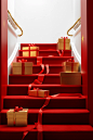 Red ribbon leading down stairs with red boxes, in the style of gold leaf accents, minimalist sets, piles/stacks, festive atmosphere, ready-made, wrapped, 32k uhd