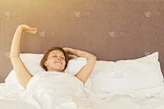 黑发女郎醒来后在床上伸开双手，太阳耀斑。晚上睡个好觉后，女孩带着快乐和放松的表情进入一天。