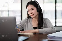 年轻的亚洲女大学生戴着无线耳机在笔记本上写学习语言，在线观看和听讲师讲课，通过视频电话在家里在线学习