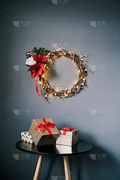 现代圣诞花圈由树枝编织而成，珍珠和灯放在灰色的墙上，桌上摆放着礼盒。极简主义节日家庭装饰。北欧风格。