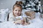 小女孩坐在圣诞树旁的地板上，手里拿着圣诞礼物。