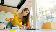 美丽的年轻亚洲女商人微笑愉快。在她的家庭办公室用包裹盒子接收客户订单。在线商业理念和交付