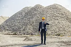 一位戴着头盔，手里拿着笔记本电脑的企业元老站在施工现场，一边看着手表，一边等待合作伙伴。商人在等着开