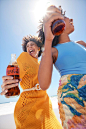 This may contain: two women standing on the beach holding up bottles of soda and smiling at each other