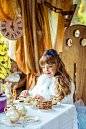一个美丽的小女孩在爱丽丝梦游仙境的风景在桌子上拿着一杯茶