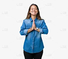 年轻美丽的黑发女人穿着蓝色牛仔衬衫在孤立的背景祈祷与双手一起请求原谅自信的微笑。