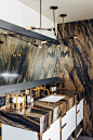 The same dark stone treatment that covers most of the walls in this master bathroom also forms the vanity countertop. The earthy print gives the space an authentic connection to nature. Metallic fixtures and accents counterbalance the natural look with st