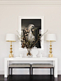 White and gold lamps on top of a white table with a glass vase and black and white wall art: