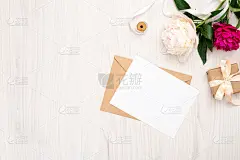 平铺牡丹花，工艺信封，空白纸卡，礼品盒，丝带木质背景。俯视图女性工作空间，婚礼请柬模型，温柔的最小组