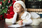 风趣的女孩在圣诞老人帽子圣诞节树附近给圣诞老人写封信