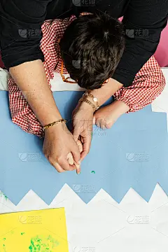 特殊教育的老师和学生穿着长袍，在桌子上用手画着生日花环和涂着丙烯颜料的黄色纸板。塑料工艺疗法。