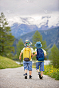 两个孩子，男孩兄弟，走在瑞士阿尔卑斯山的一条小路上，背着背包爬山，采集草药和鲜花
