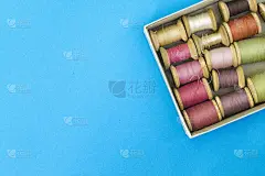 彩色的缝纫线在蓝色背景上以一排渐变的方式放在盒子里。这里有文本的位置。