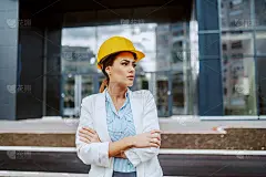 年轻自信有吸引力的白种年轻女建筑师站在户外双臂交叉，等待建设者的到来。