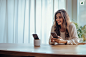walterssaucedo_A_young_woman_sits_at_a_table_phone_in_hand_smil_55e984e8-38d8-43f8-8c7d-8bc2310598dd