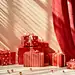 Gifts with red boxes and gold foil on a shelf, in the style of scattered composition, luminous hues, monochromatic abstractions, polka dot madness, light red, tabletop photography, stripes and shapes