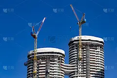 两座建筑吊车依附在一座现代高层建筑的建筑背景上，明亮的蓝天衬托着高层建筑。