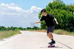 一位身穿黑色衬衫和裤子的年轻亚洲男子正在乡村公路上玩花样滑冰。在阳光明媚的日子里，玩冲浪溜冰