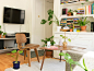 Modern living room with wooden furniture, plants on the floor, a tv on the wall, and bookshelves in the background