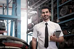 肖像微笑的商人卖家站着和持有数字平板电脑在汽车配件商店商店仓库与许多二手发动机零件模糊的背景。