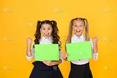 家庭作业完成。快乐的小孩拿着黄色的背景的空作业单。可爱的小女孩微笑着与空白的绿色学校海报的家庭作业作