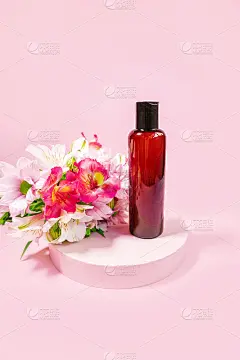 深色玻璃化妆瓶上粉红色的背景装饰有花。表示海报。带有文本位置的横幅。空间的文本。化妆产品的模型。洗头