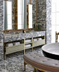 Heavily figured marble, gold accents, a triptych in mirrors above a beautiful double vanity, a black enameled freestanding bathtub, and a tufted, contoured bench to match