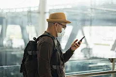 戴口罩的年轻旅行者可以保护流感冠状病毒。旅客在机场候机楼用智能手机等待航班。在大流行期间必须保持社交