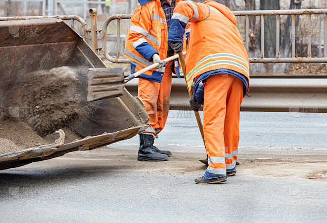 道路工人用铲子将车道间堆积的沙子铲掉，然...