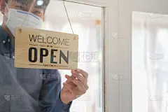 年轻的企业主戴着口罩和开业标志。