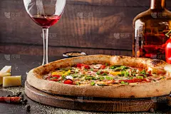 意大利美食概念。一个真正的披萨，有蔬菜、火腿、培根和帕尔马干酪。配料摆在桌上。桌上有杯红酒。特写镜头