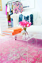 Lucite nesting tables as coffee tables, pink Persian rug, white sofa, orange books, and clothing rack