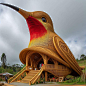 "Hummingbird House" is a cozy, whimsical abode nestled amidst a lush garden, adorned with vibrant blooms and swaying trees. Its quaint exterior boasts intricate wooden details and inviting hues. Inside, sunlit rooms are adorned with charming dec