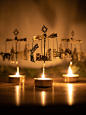 Three nativity themed brass rotary candleholders on a white marble table with pine garland in the background.