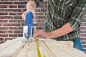Carpenter cutting wooden plank with electric saw against red brick wall