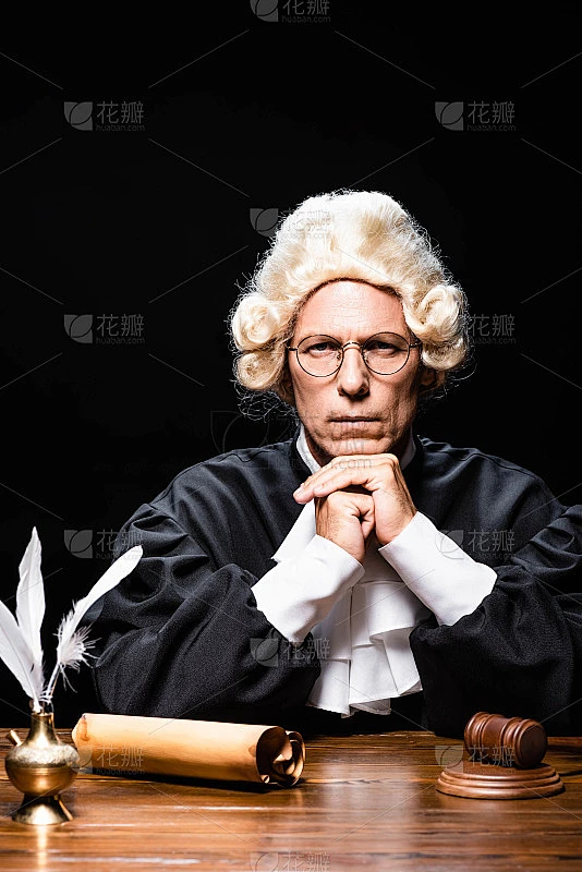 严肃的法官身穿法官袍，头戴假发，望着孤立的黑色摄像机素材-花瓣网