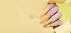 女性手与黄色指甲设计。长指甲。女人手在黄纸背景上。