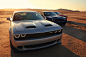 Three 2021 Challenger muscle cars parked on a desert plain. The low sun casts dramatic shadows.