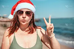 一个戴着圣诞帽、穿着泳衣的快乐女孩的肖像，她用手做着和平的手势，并对着镜头飞吻