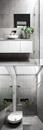 这个现代主浴室有一个覆盖着墙壁和地板的大灰色瓷砖。 玻璃隔板将淋浴与白色浮动盥洗台分开，并且天窗为房间增添了充足的自然光线。