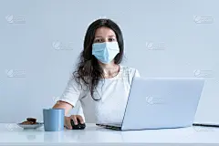 这个女孩在隔离期间在家工作。冠状病毒大流行。一个戴着外科口罩的女孩一边用笔记本电脑工作一边喝咖啡。遥