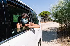 在新冠肺炎大流行期间，一个棕色头发的矮胖女孩，戴着面罩和太阳镜，从车窗向外张望，正在松树路上度假