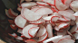 Slices of radish fall into black salad bowl