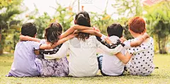 后视图，一群幼儿园的多民族小朋友在公园户外围成一圈坐在一起，展示了童年的友谊，团结与多样性。